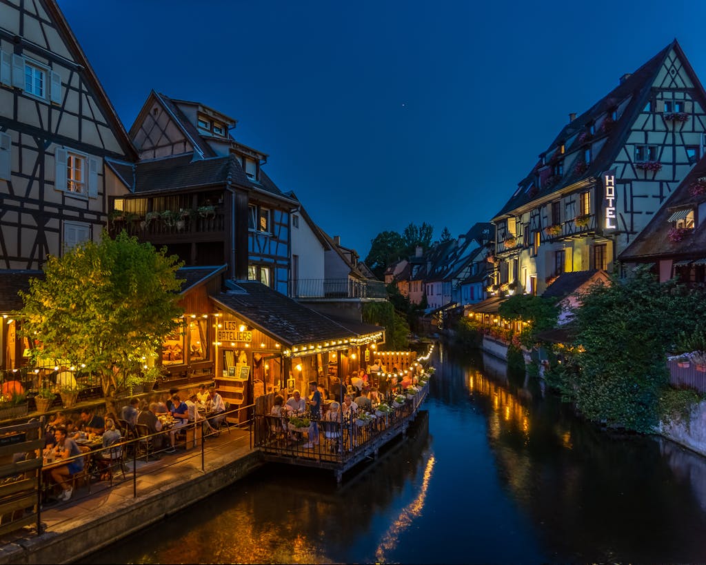 Nighttime view of Colmar's timbered houses and canal-side dining, beautifully illuminated.